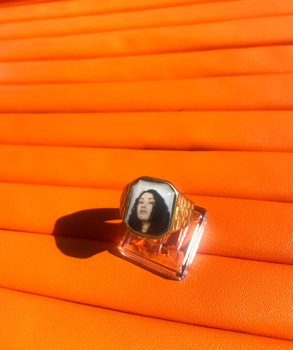18K gold-plated Cleo Sol-inspired Lav Vintage promise ring with square face, photographed on an orange background.
