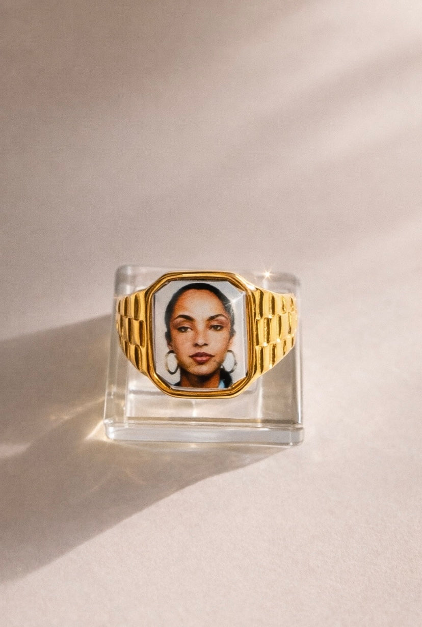 Square 18K gold-plated promise ring featuring a Sade-inspired portrait, styled on a soft neutral surface.