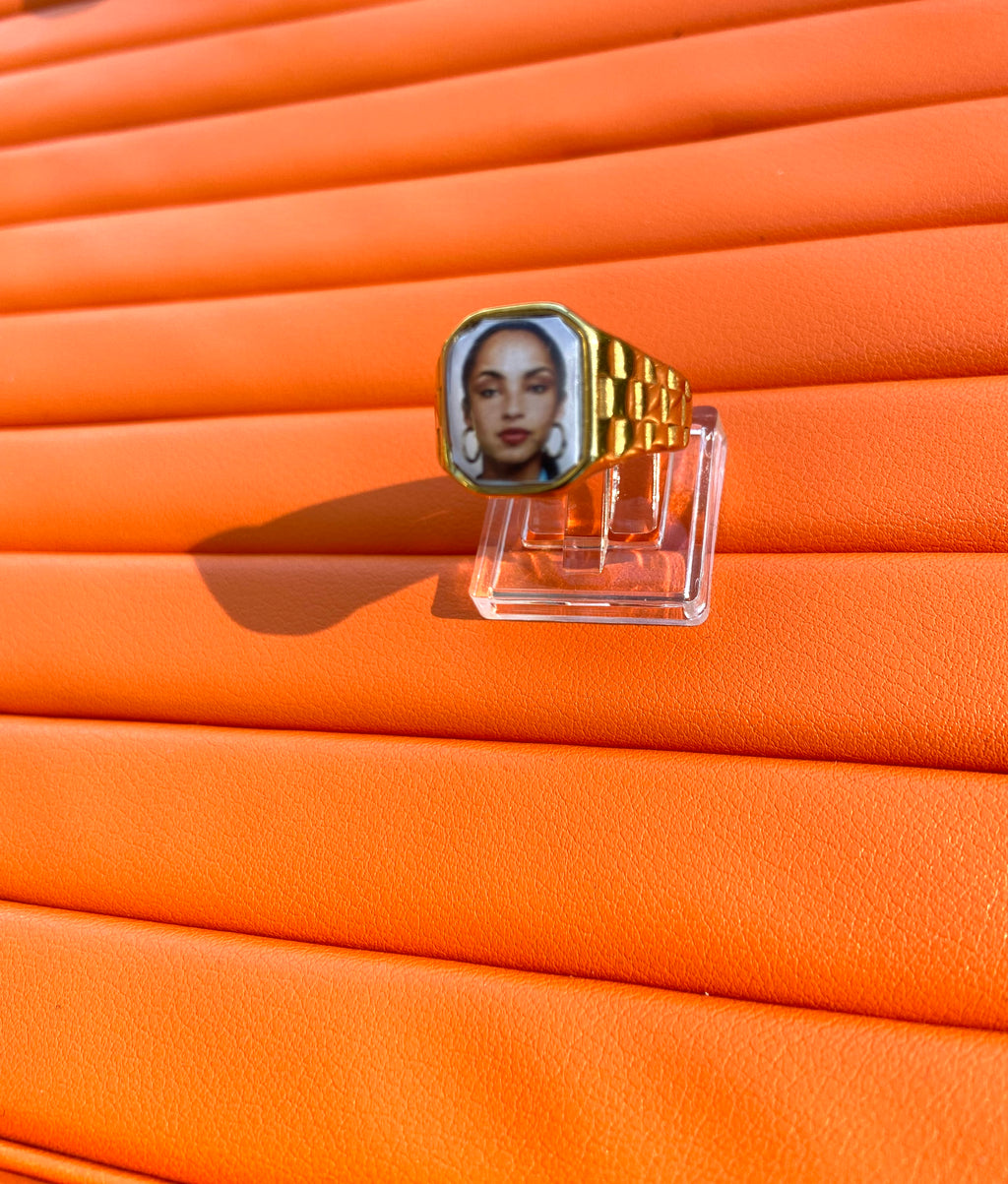 Square 18K gold-plated promise ring featuring a Sade-inspired portrait, styled on a soft neutral surface. Orange background 