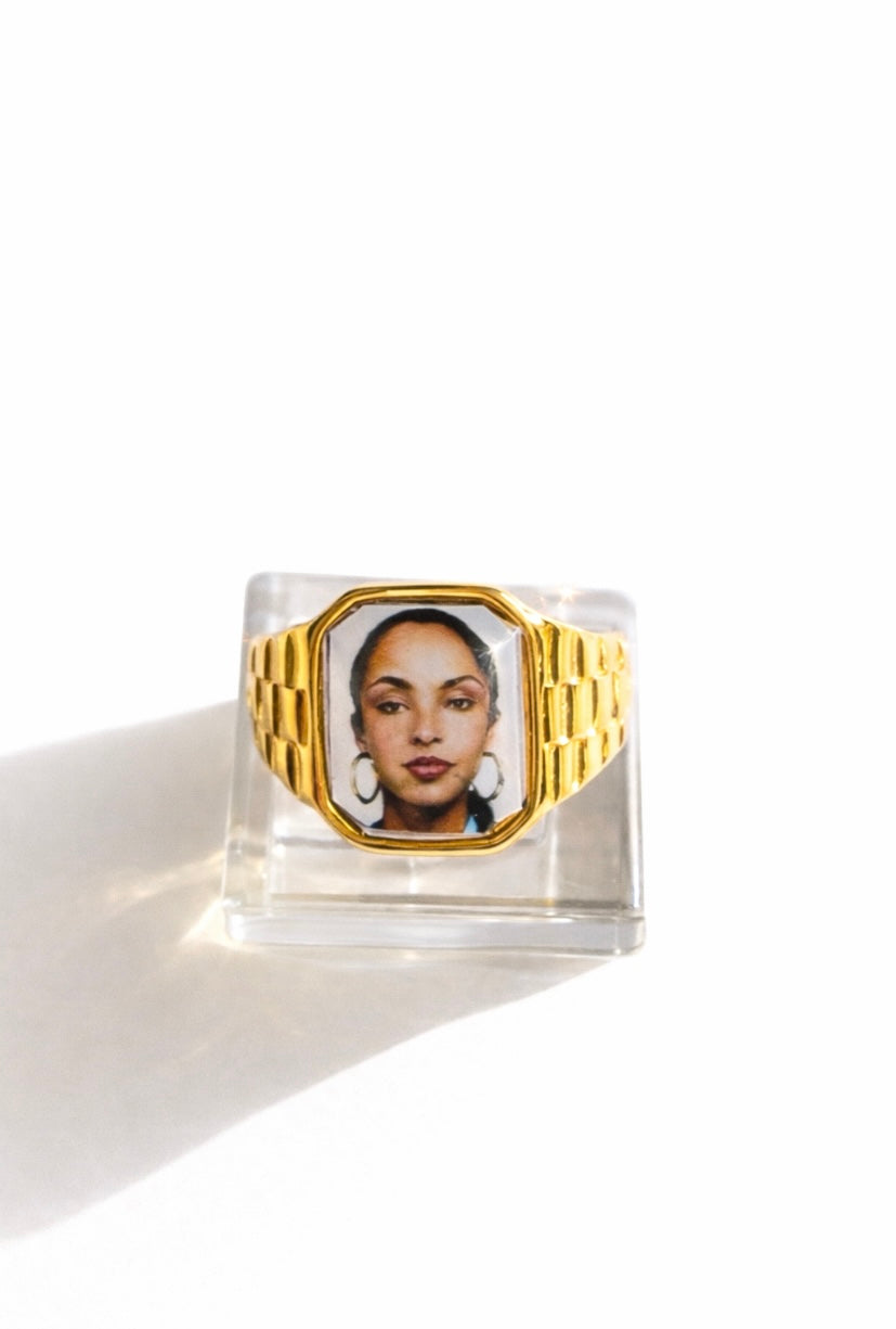 Square 18K gold-plated promise ring featuring a Sade-inspired portrait, styled on a soft neutral surface.