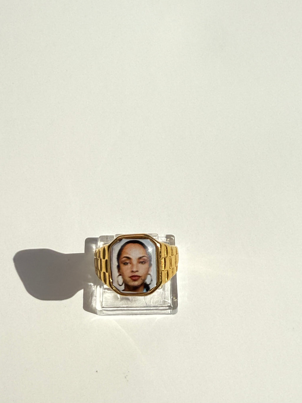 Square 18K gold-plated promise ring featuring a Sade-inspired portrait, styled on a soft neutral surface.