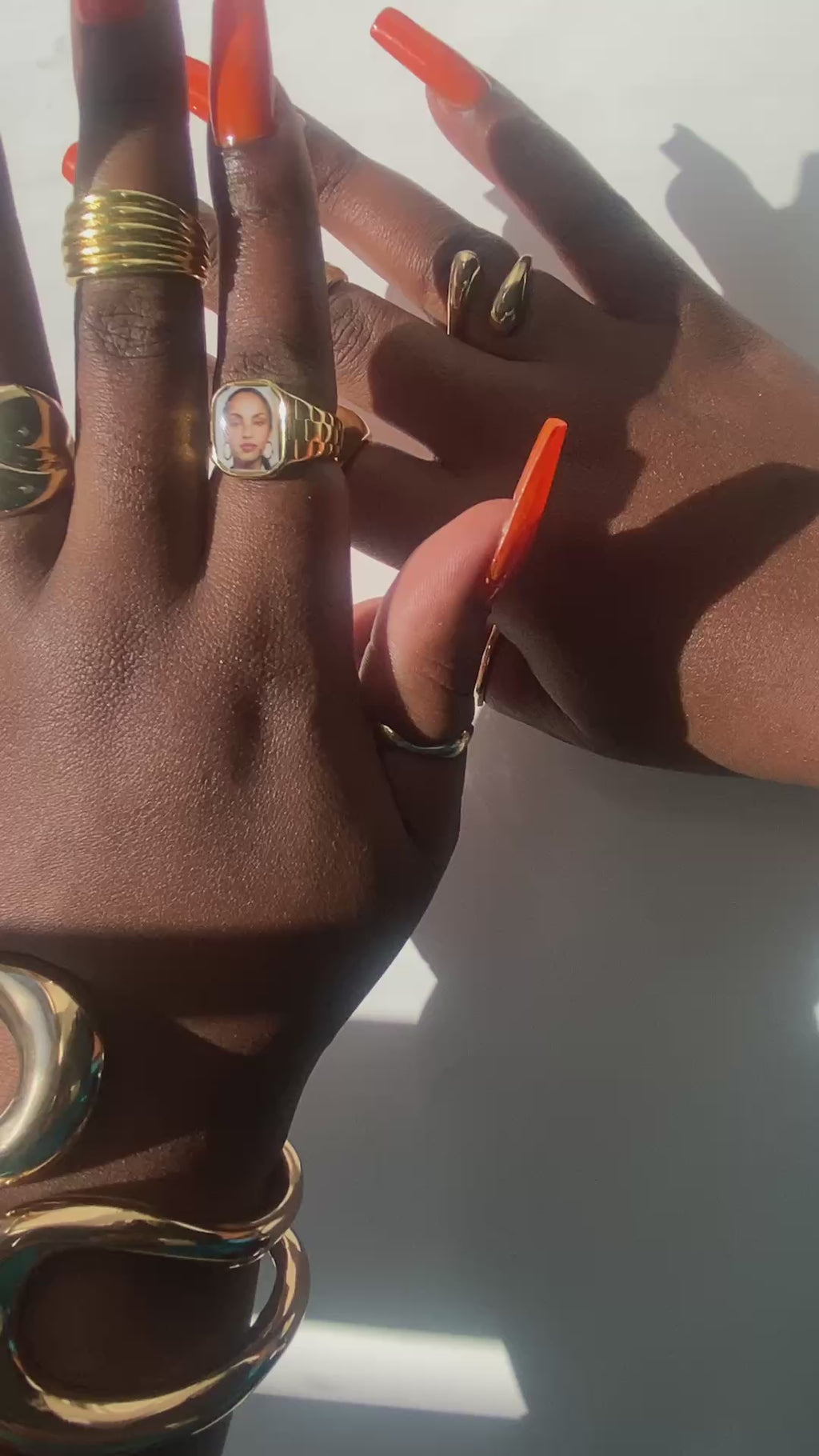 Video showing Hand wearing stacked gold rings and sculptural gold cuffs, including a square Sade-inspired promise ring, styled in natural sunlight.