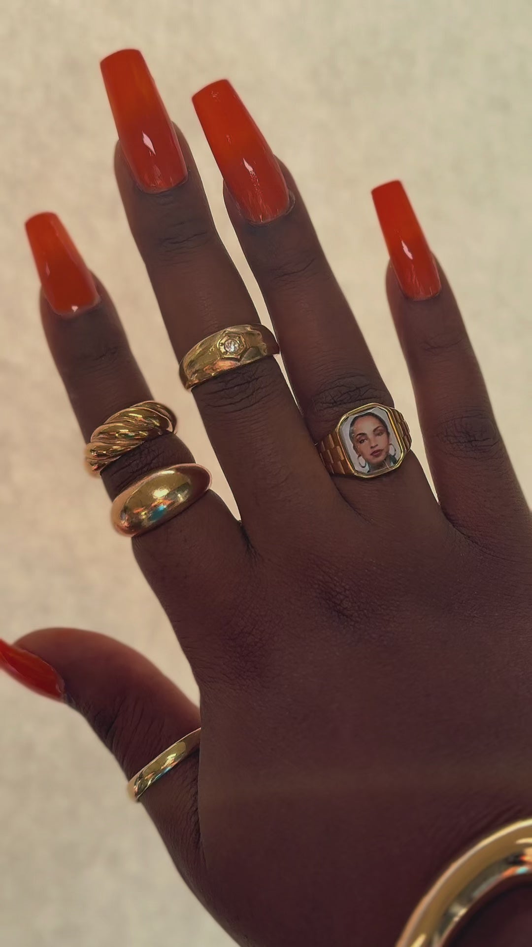 Video showing Hand wearing stacked gold rings and sculptural gold cuffs, including a square Sade-inspired promise ring, styled in natural sunlight.
